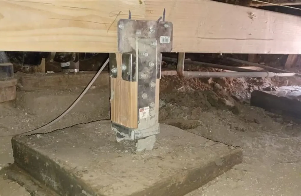 steel post cap and post base bolted to a wood post on a concrete pier in a crawl space during a seismic retrofit