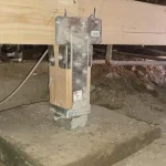 steel post cap and post base bolted to a wood post on a concrete pier in a crawl space during a seismic retrofit