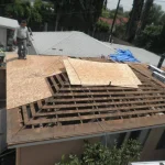roof tear-off exposing the rafters with new plywood decking being installed over the old skip sheathing