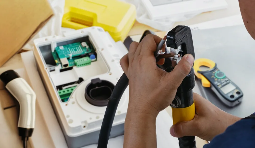 technician crimping the cable on an EV charger with the enclosure open and a clamp meter on the bench