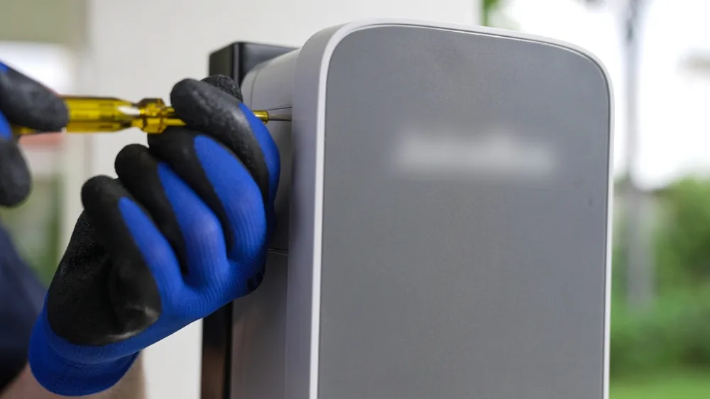 Electrician in gloves fastening a wall-mounted EV charger with a screwdriver